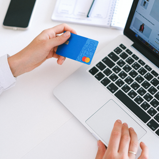 Person sitzt vor einem Laptop und hält Kreditkarte in der Hand für die Bezahlung des Onlineshoppings